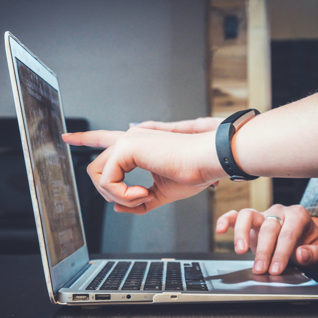 Open laptop with one hand pointing to the screen and another hand on the touchpad