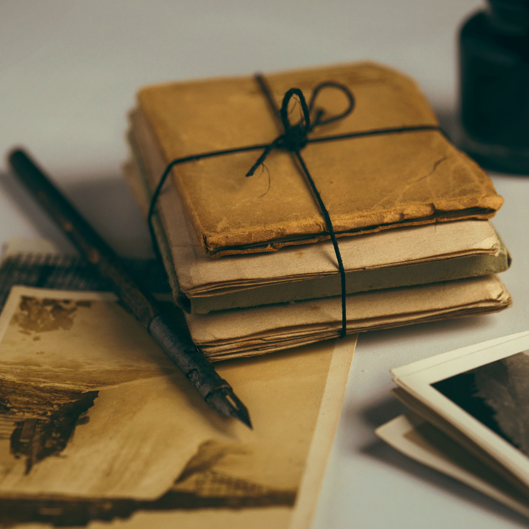 A tabletop with a packet of papers and booklets, tied with string, and a fountain pen and old photos